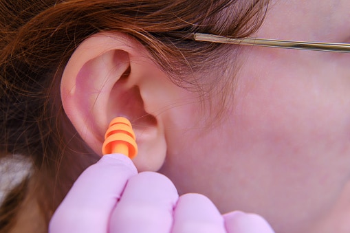 A woman inserts earplugs into her ear.
